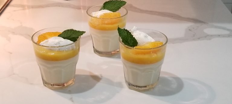 Photo of three panna cottas topped with orange curd, an orange surpreme, a dollop of whipped cream, and a mint leaf.